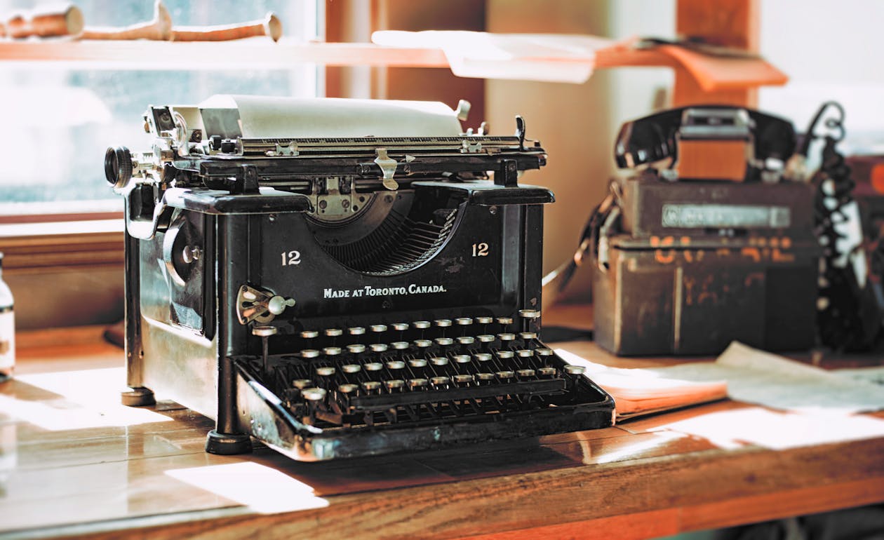 Vintage typewriter and rotary phone on a wooden desk for cozy mystery writing