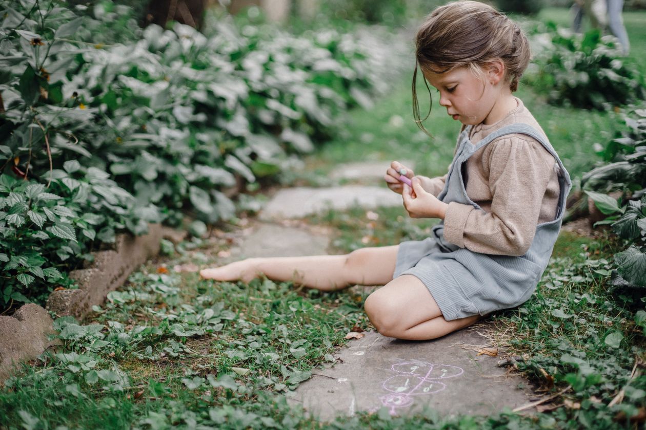 Young girl playing a chalk writing game on a garden path