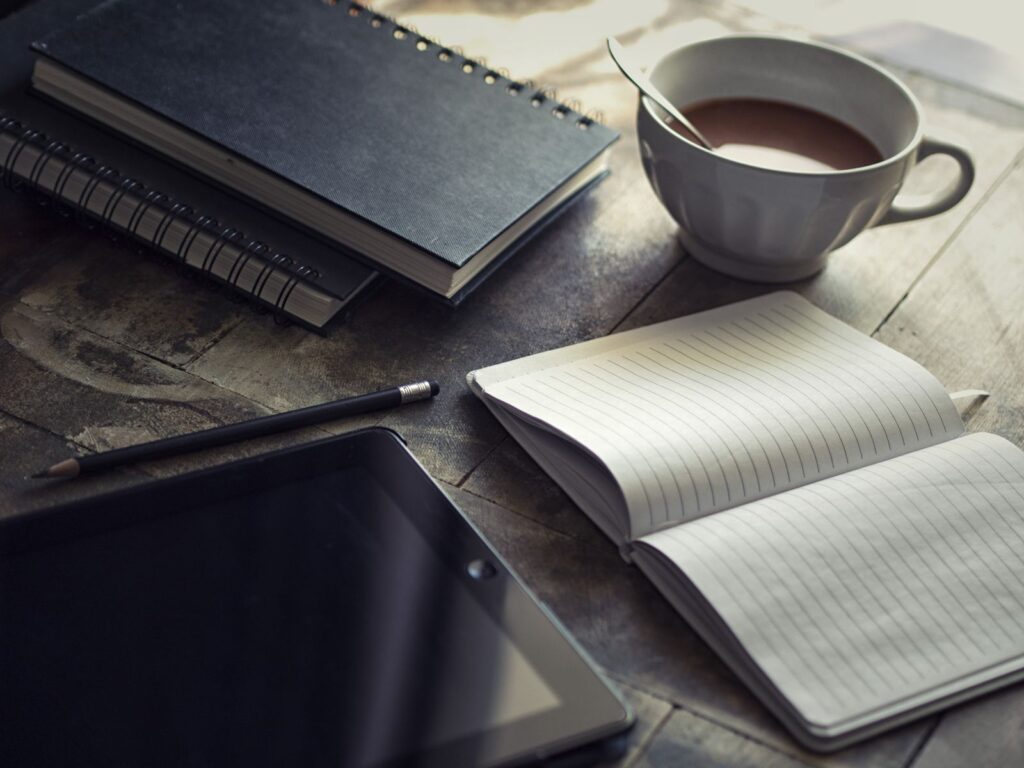 Books, notebook, and coffee on a writer’s wooden desk