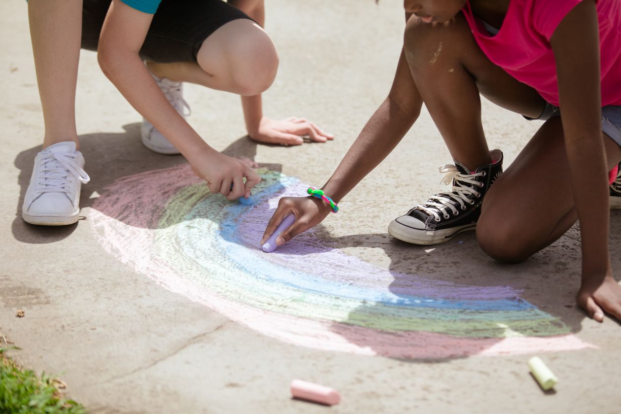 Kids drawing a chalk rainbow on a sunny sidewalk
