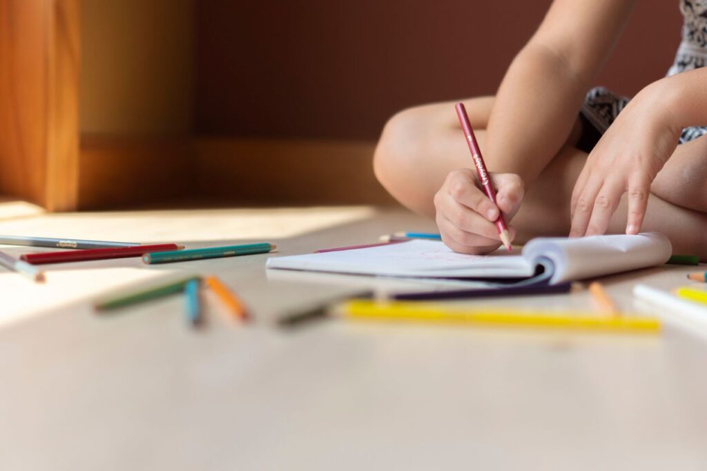 Child writing in a notebook with colored pencils in summer light