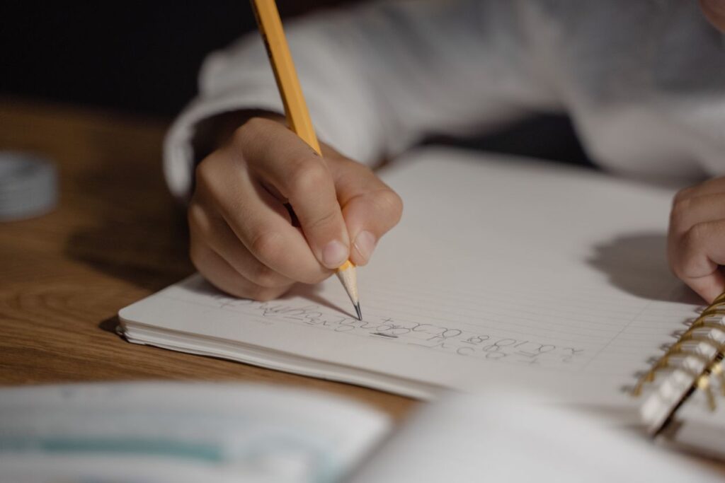 Child writing homework in a spiral notebook with a pencil